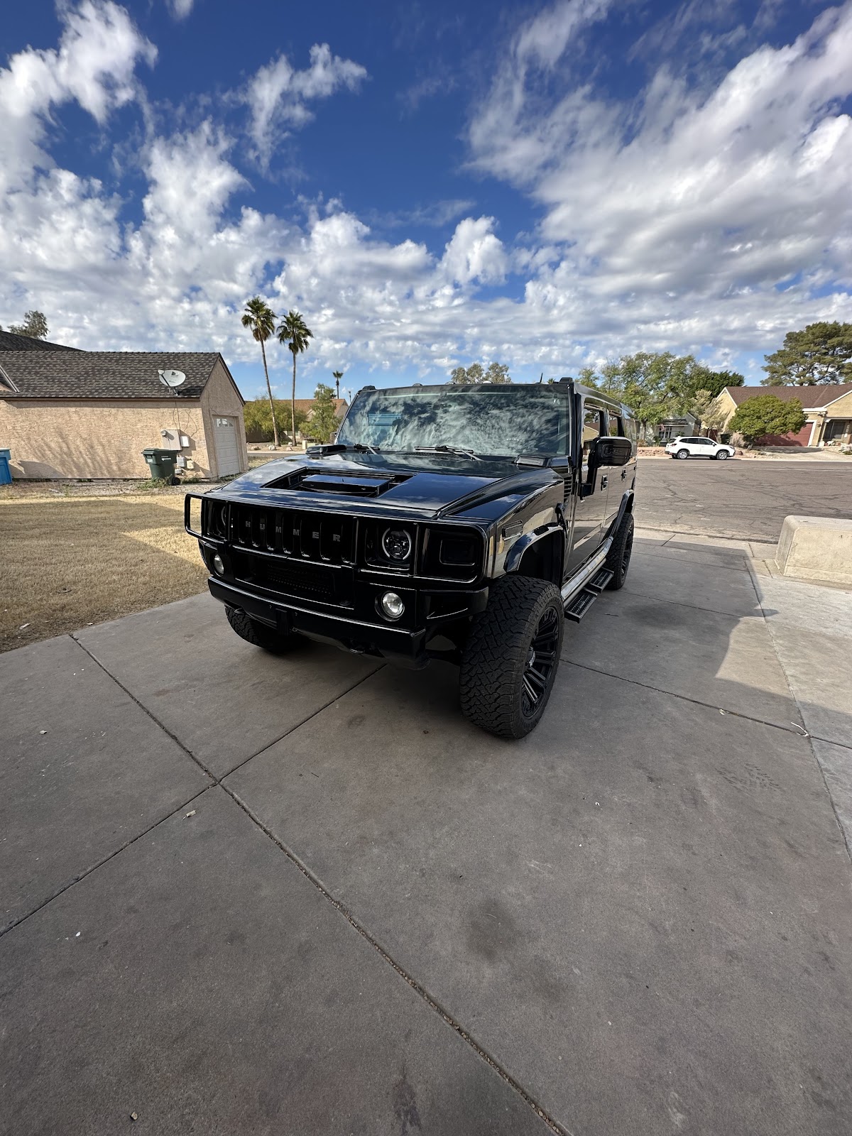 Black 2007 Hummer H2 parked on a concrete driveway under a bright Arizona sky, palm trees and neighborhood houses behind it